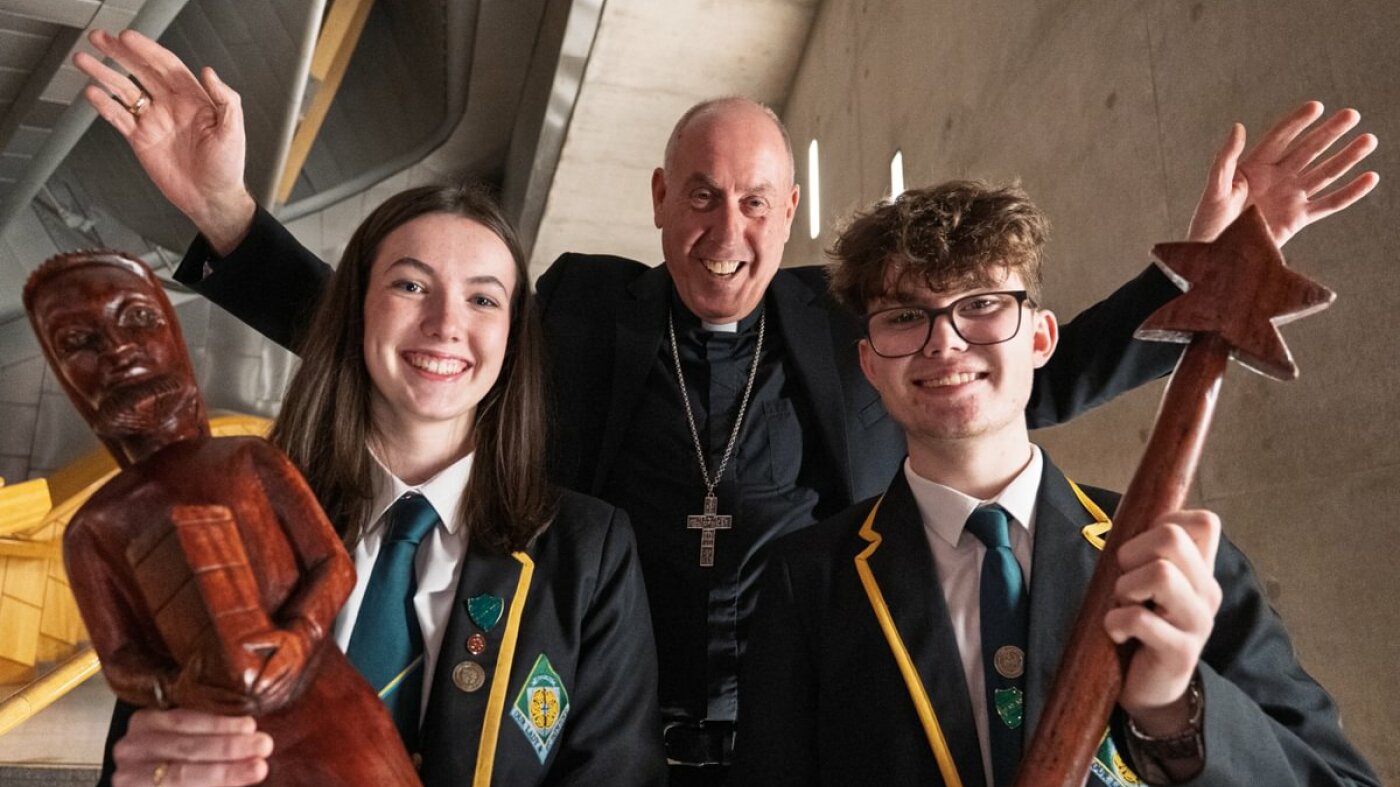 Bishop Brian McGee and two school pupils smiling at the camera holding wooden nativity figures. 