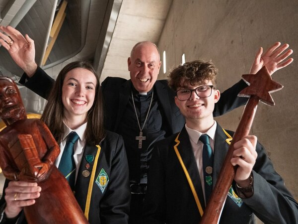 Bishop Brian McGee and two school pupils smiling at the camera holding wooden nativity figures. 