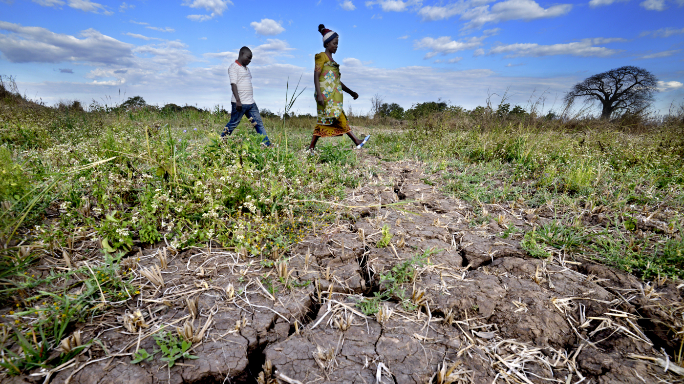 Gabriel and Ethel walk over very dry grass and earth, Malawi. Their crops were destroyed by Tropical Storm Ana in January 2022.